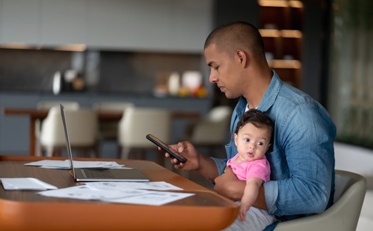 Busy Latin American father multi-tasking while taking care of his baby at home during lockdown - par...