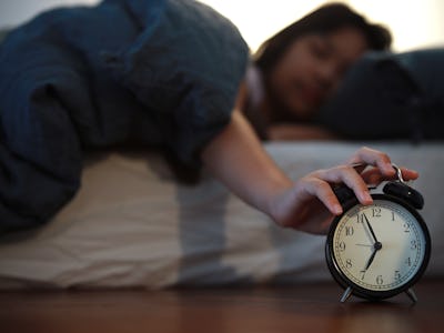 Upon waking up early in the morning, a young Asian girl tried to turn off the alarm clock in her bed...