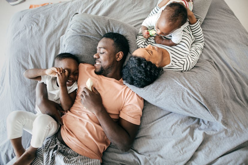 A mom, dad, and two young kids play in bed, in a story about Father's Day Facebook post ideas.