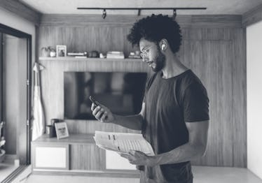 Brazilian man at home taking a call from his bank and using earphones while holding his bank stateme...