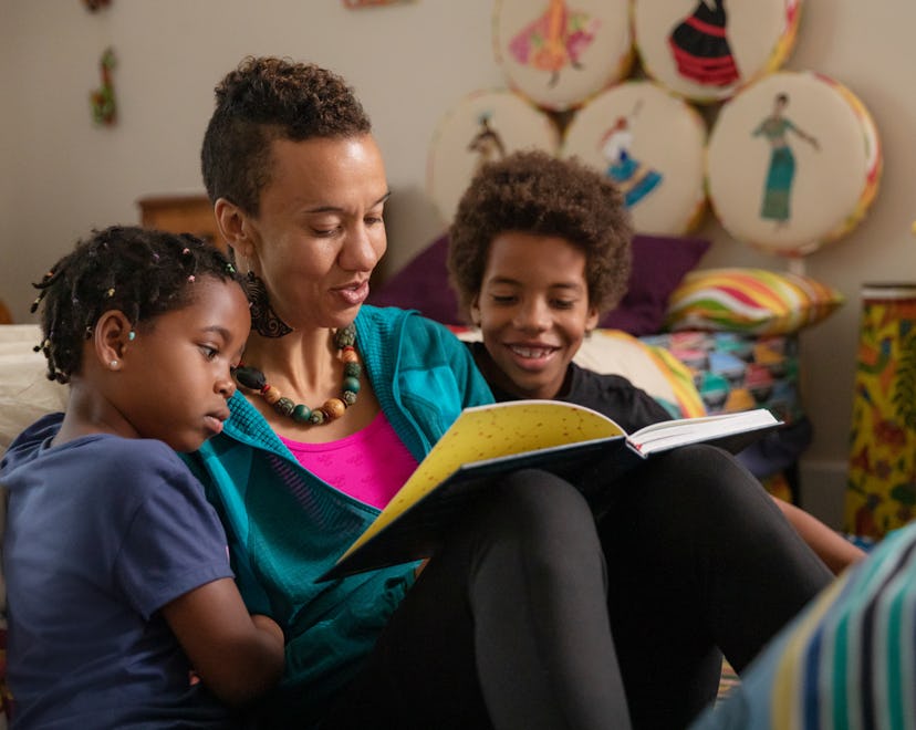 A woman reading a bedtime story to her son and daughter as they are gathered around her