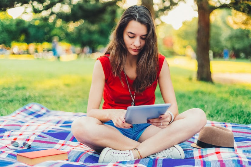 Young girl resting and reading an e-book in the city park