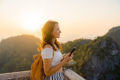 Young Caucasian woman  standing on the top of wat Tham Sua in Krabi at sunset and using smartphone