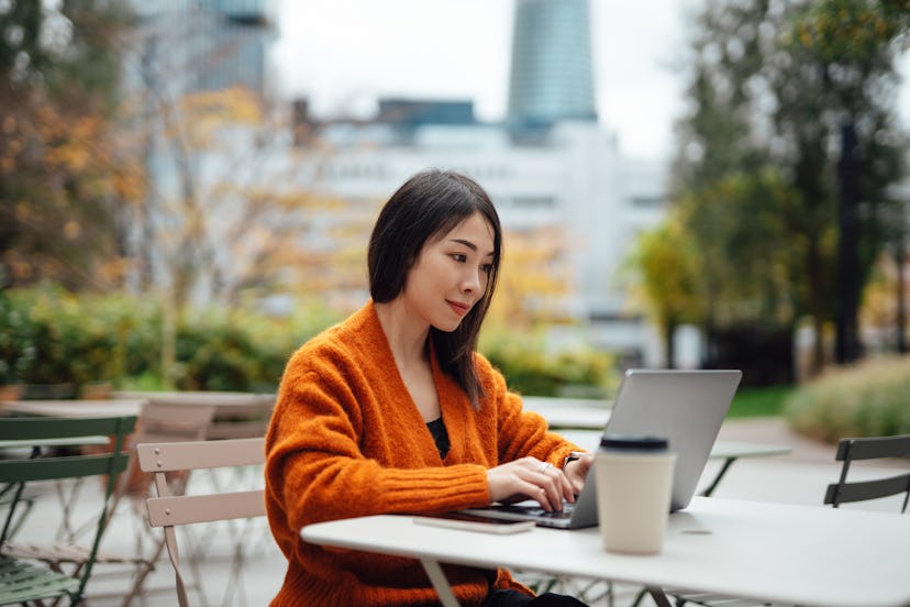 Young Asian business woman having a video call on laptop, sitting at outdoor cafe. Remote working. F...