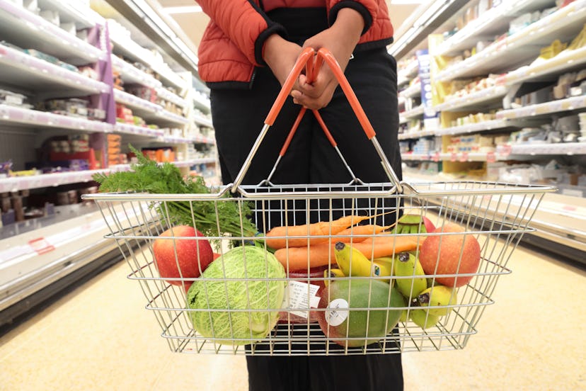 woman holding shopping basket of fruit and vegetables in supermarket