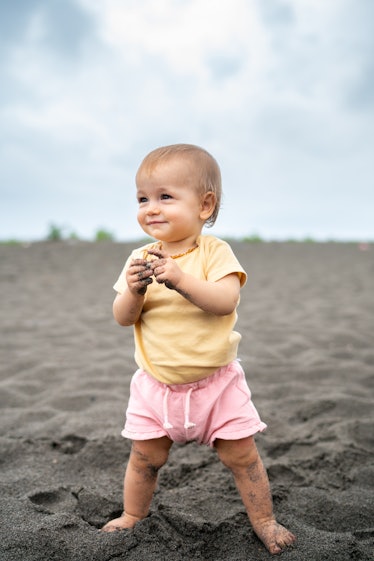 Cute baby girl playing in the sand on the beach during summer day