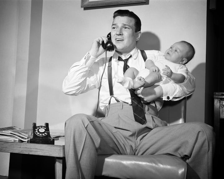 1950s distressed father holding baby while talking on telephone. (Photo by Debrocke/ClassicStock/Get...