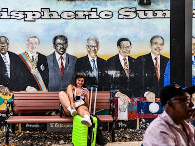 A woman sits on a bench near a mural of South American leaders at Domino Park, located in a Cuban ne...