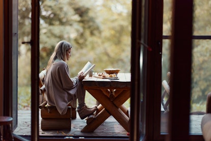Young woman reading a book while relaxing on a patio in autumn day. Copy space.