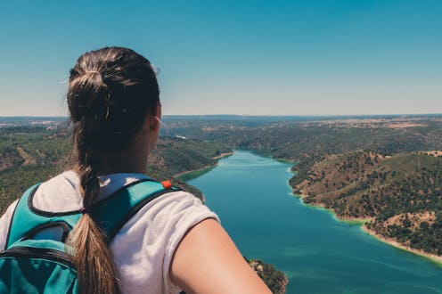Blonde girl with braid looking at a beautiful mountain and lake landscape in Monfrague national park...