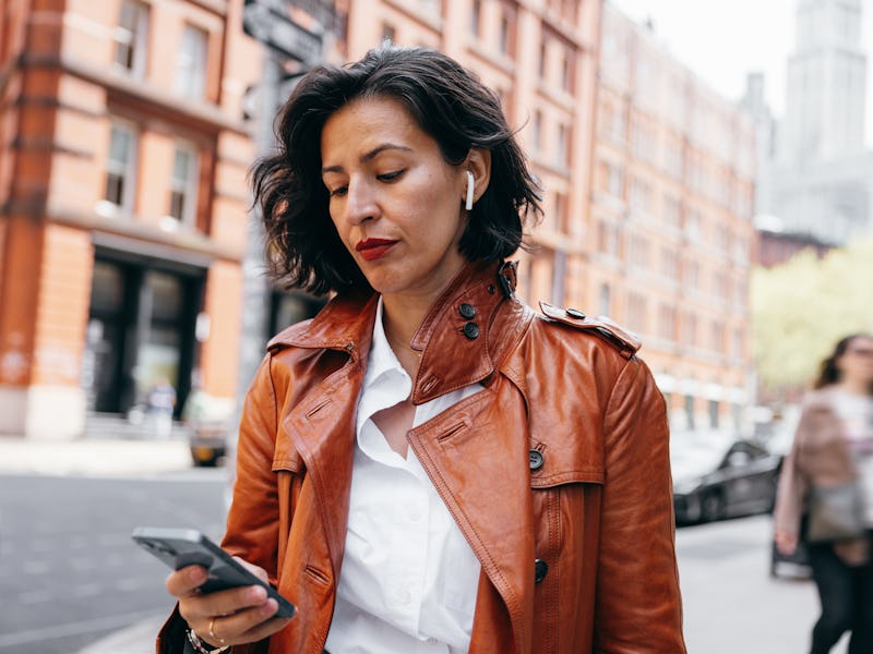 Elegant businesswoman walking to the office listening voice messages on earphones in downtown New Yo...