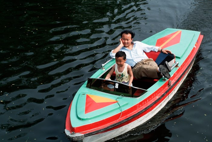 SHANGHAI, CHINA - 1994/05/01: A father lets his son drive a small rented toy speed boat on a recreat...