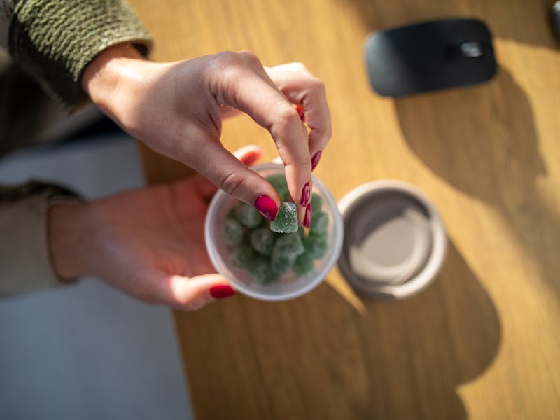Unrecognizable woman working in her home work space. She is taking a CBD gummy candy from a plastic ...