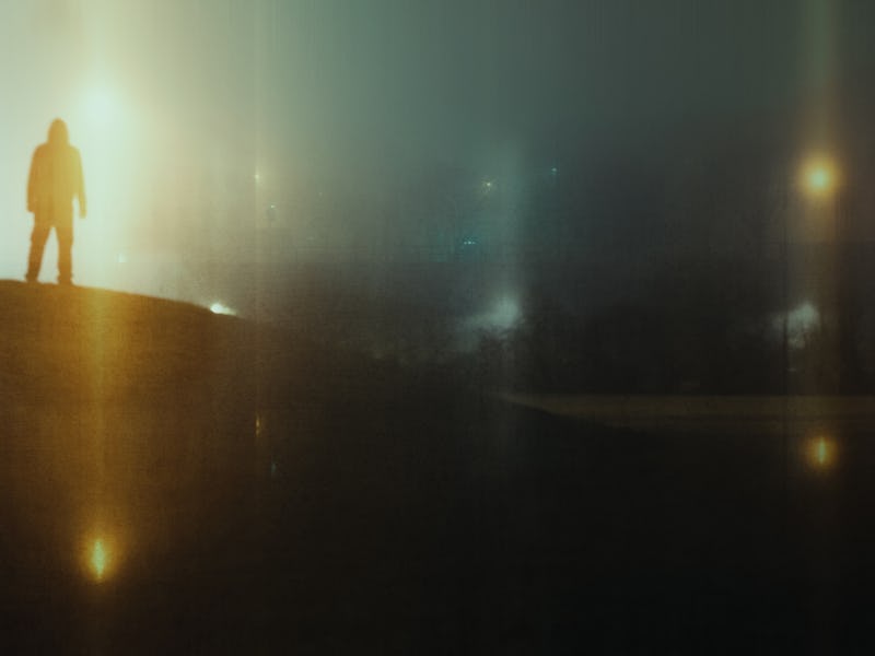 A man standing on a hill looking at glowing UFO lights in the sky. With a blurred, grunge edit.