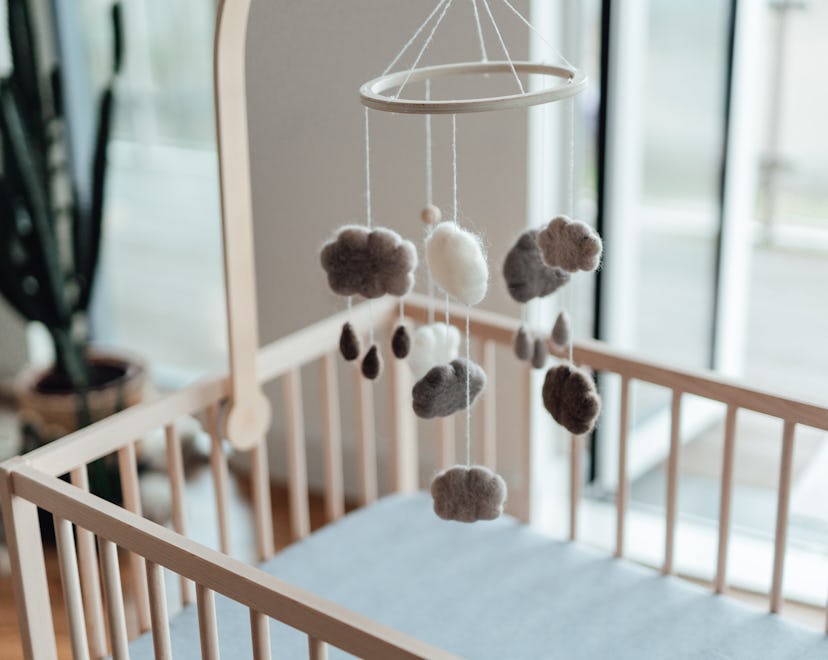 Stylish Scandinavian newborn baby nursery with natural wooden baby cot and handmade mobile hanging o...