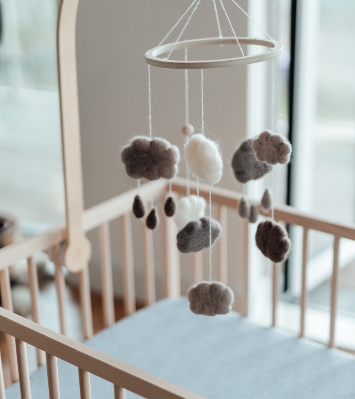 Stylish Scandinavian newborn baby nursery with natural wooden baby cot and handmade mobile hanging o...