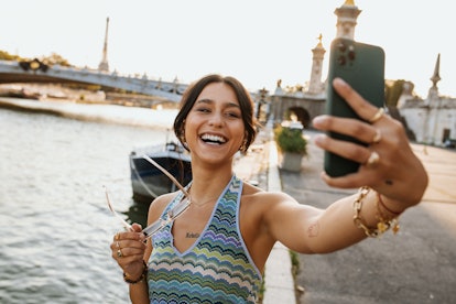 young woman smiles and takes a selfie as she enjoys vacation and considers how the July 2023 super b...