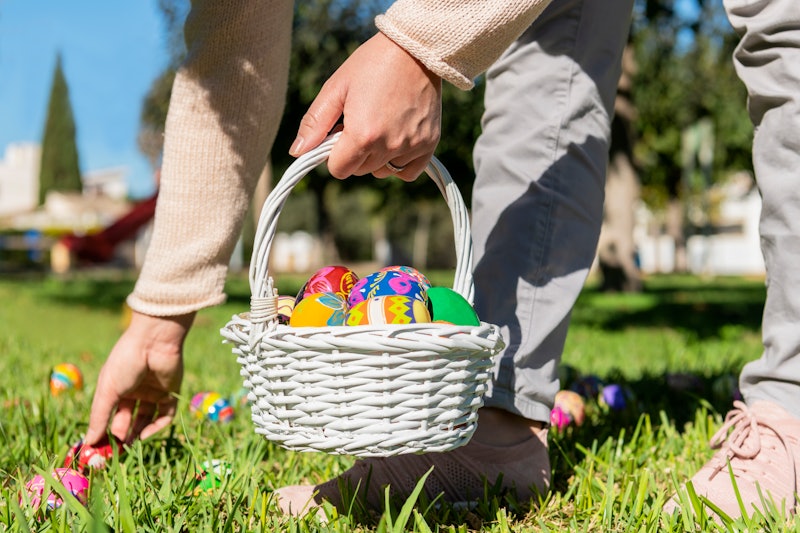 Close up of female holding an easter egg basket and hiding eggs in the grass on an out of focus back...