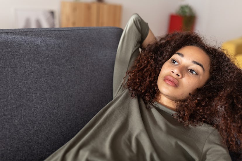 Young Latin American woman feeling confused thinking about personal life problems while resting on c...