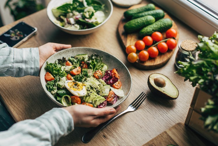 Woman mixing superfood salad ingredients with wooden spoons in kitchen.