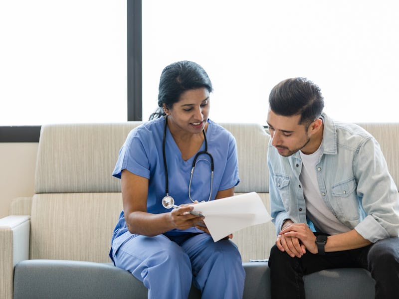 The young man and female doctor sit on the hospital room couch and review the medical chart together...