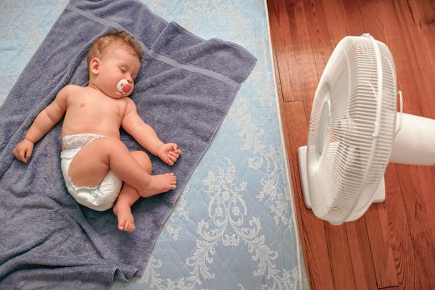 Baby lays on towel on floor in front of fan, in a story about signs your baby is overheated.