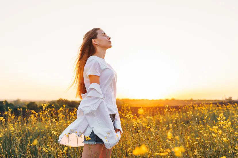 Deep breathing. Young woman with closed eyes breath deeply in a blooming field with yellow flowers a...