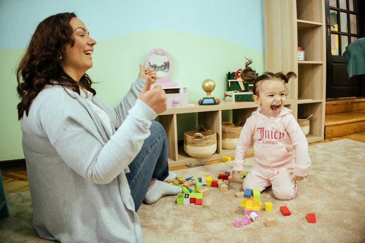 Happy teacher is playing with a girl in the kindergarten. The little girl has pigtails and is smilin...