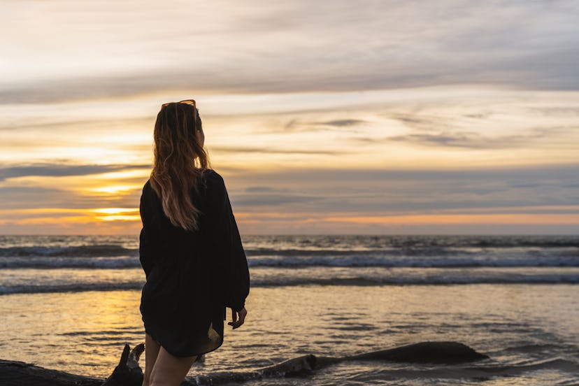 Serene sunset scene. Young woman standing on the shoreline at sunset.