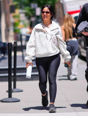 Camila Cabello wears black leggings, a gray sweater, a white Lululemon belt bag, and black sneakers....