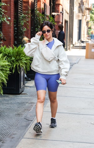 Camila Cabello wears a gray sweater, a purple bodysuit, and black sneakers. 