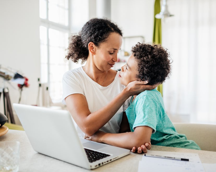 A single mom being affectionate with her young son while working from home on her laptop.