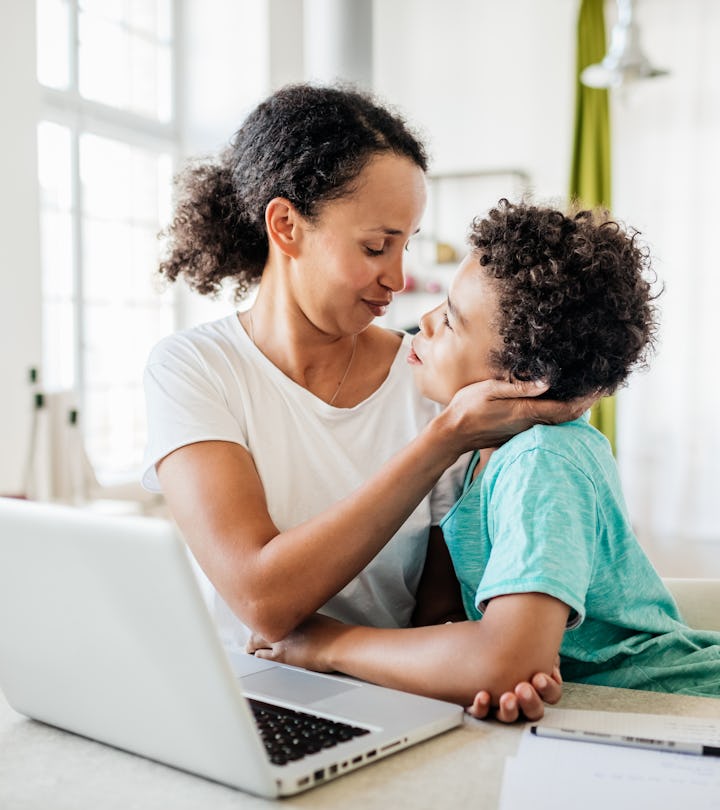 A single mom being affectionate with her young son while working from home on her laptop.