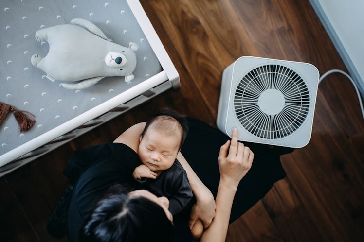 High angle shot of Asian mother turning on home air purifier while carrying her sleeping newborn bab...
