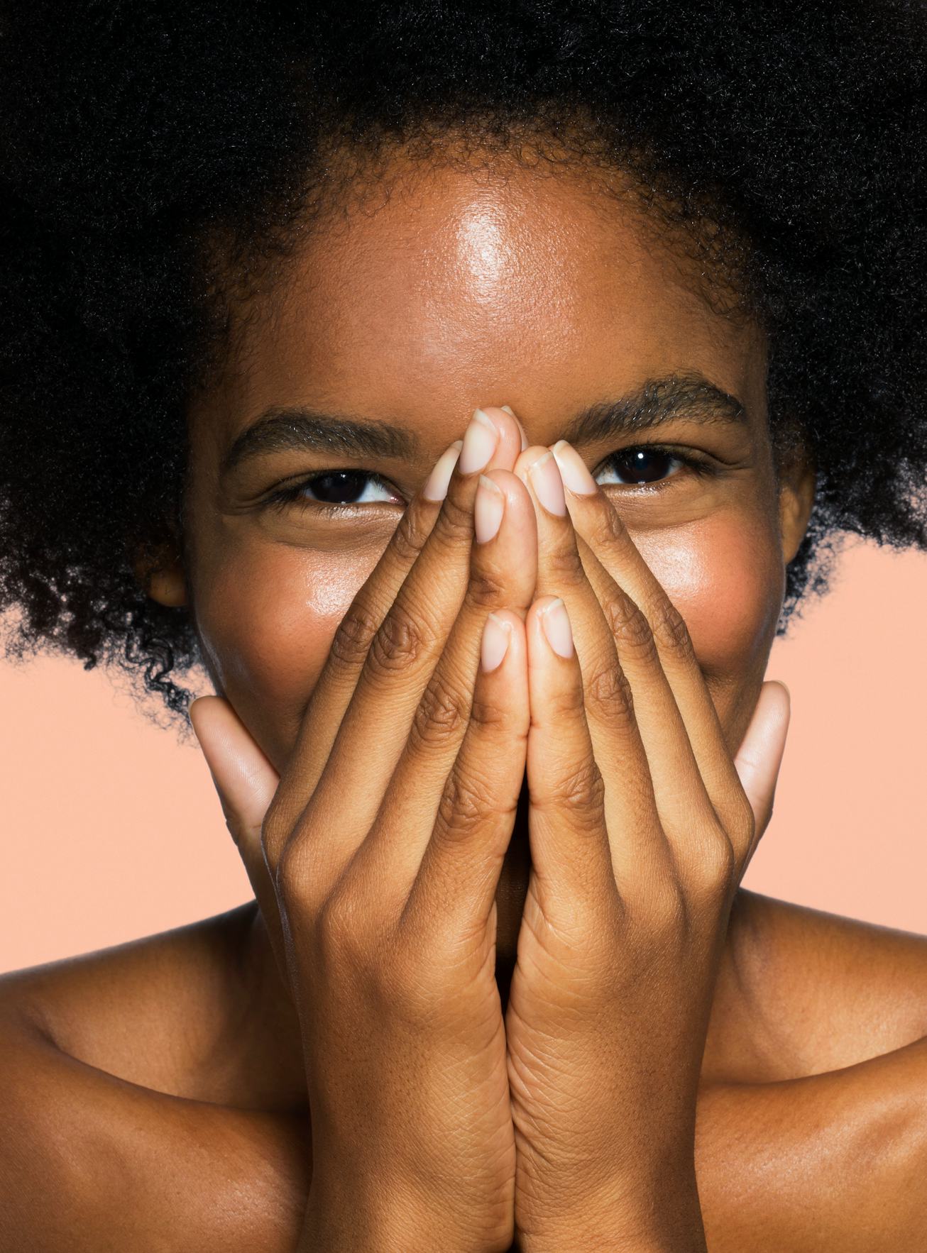 Young mixed-race female covering nose and mouth with hands with pink background
