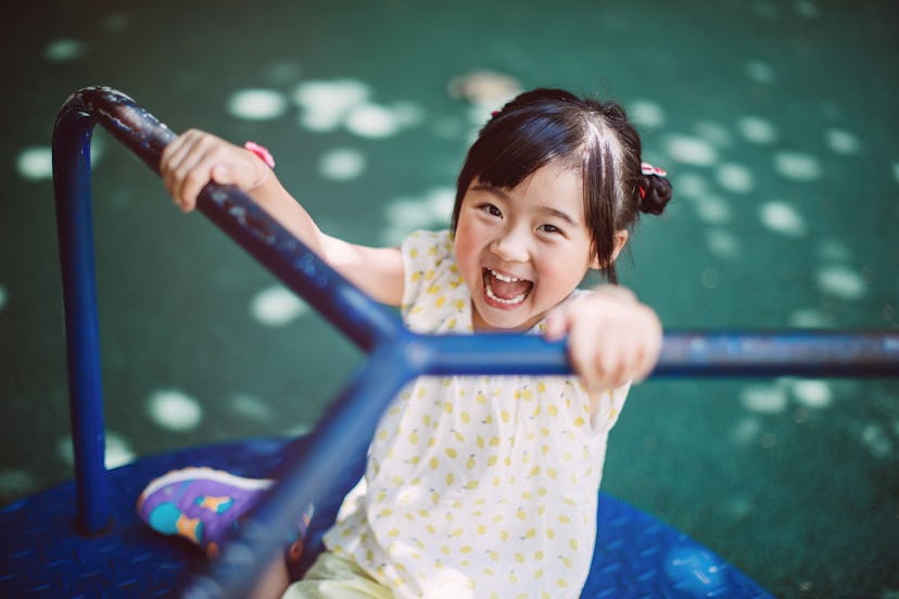 happy little girl playing on the merry go round in the playground joyfully in a roundup of kids capt...