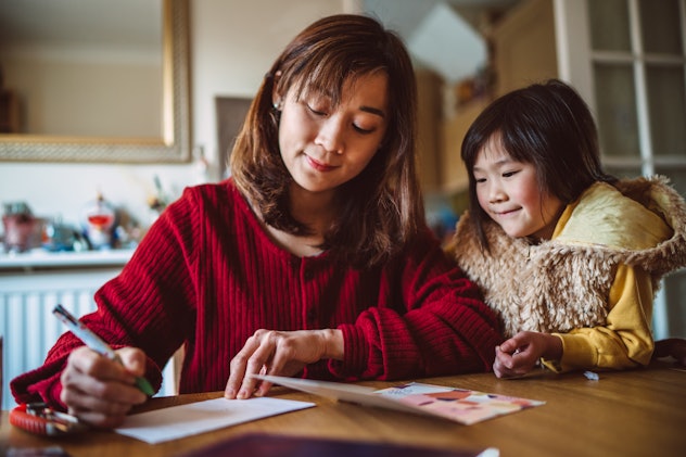 Young pretty mom filling out father's day card with a father's day message with daughter 