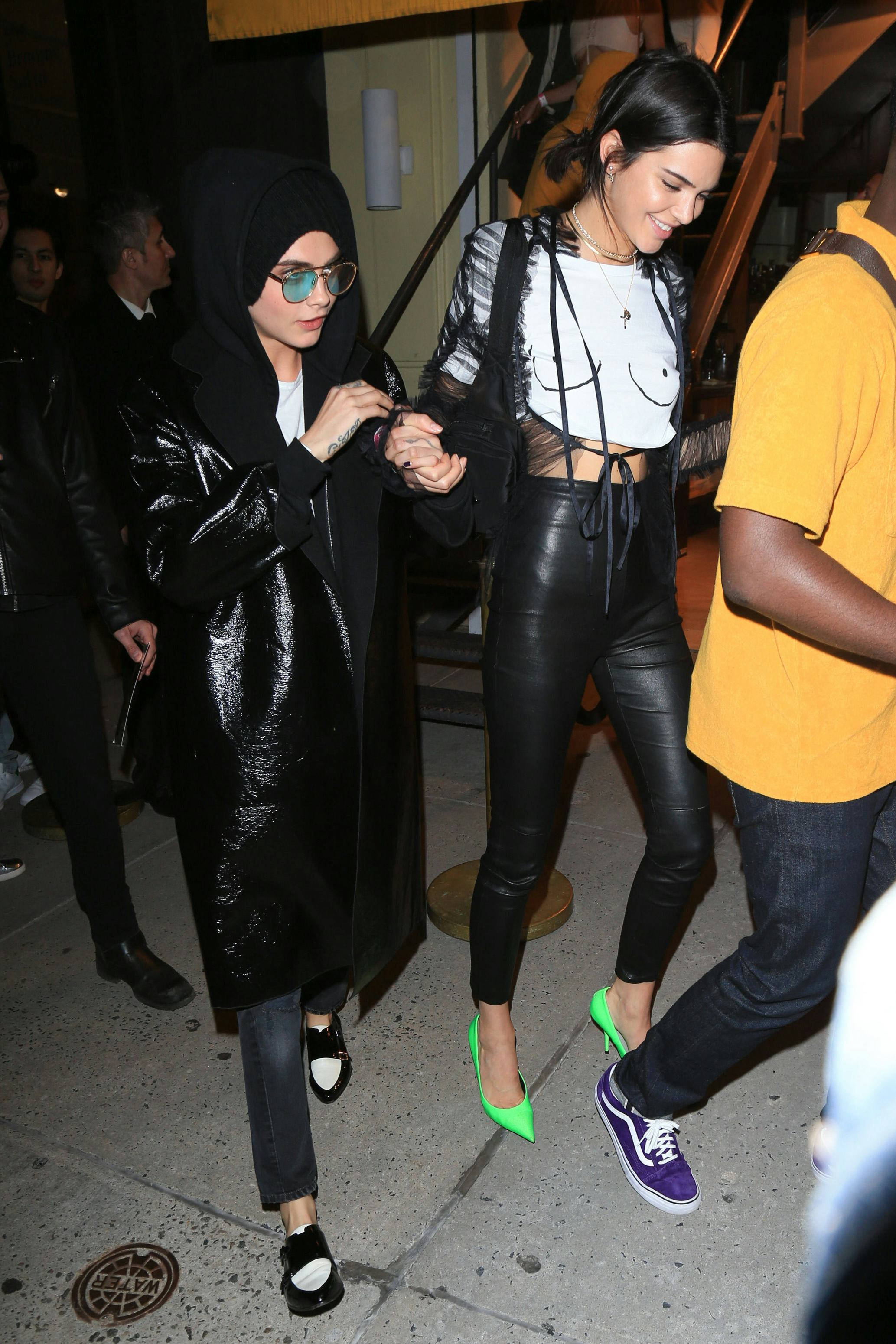 Kendall Jenner wears a boob print T-shirt by Never Fully Dressed, black pants, and green pumps. Cara&hellip;