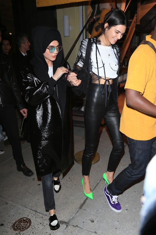 Kendall Jenner wears a boob print T-shirt by Never Fully Dressed, black pants, and green pumps. Cara…