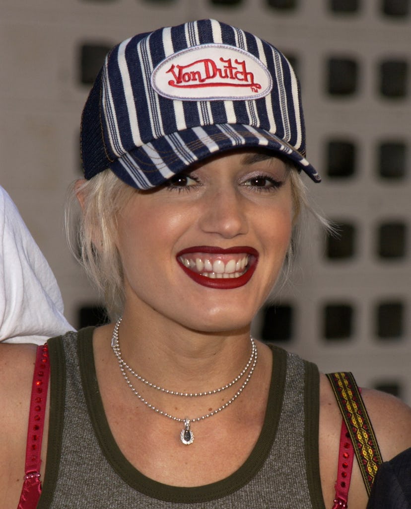Gwen Stefani wears a striped Von Dutch cap, green tank, and red straps. 