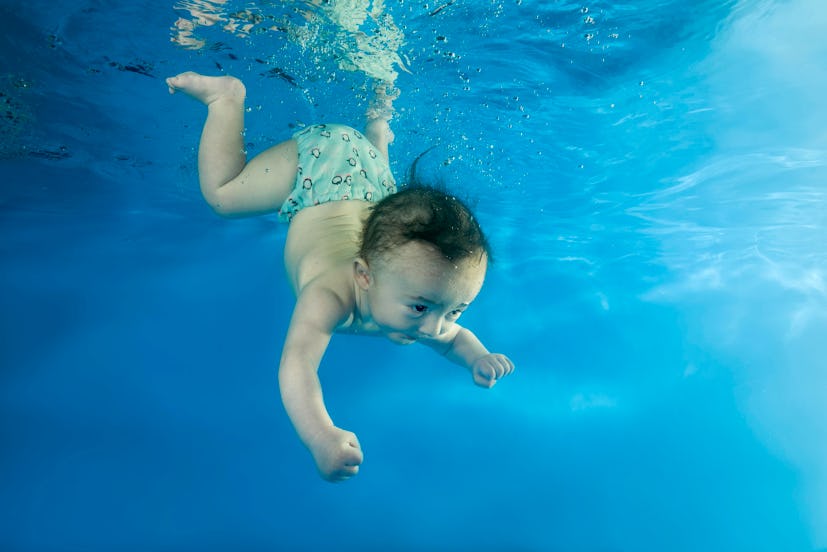 a little boy smiles as he dives and swims underwater in a blue swimsuit