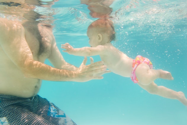 baby girl swims towards her dad underwater in pink swim trunks