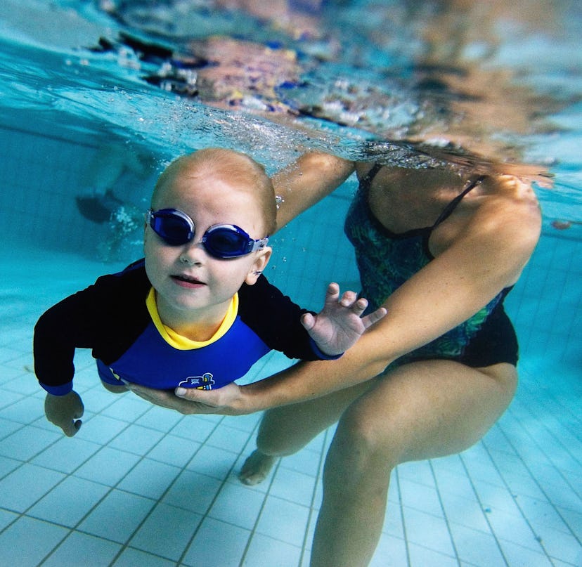 A toddler held by his mother swims underwater during a swimming class for babies