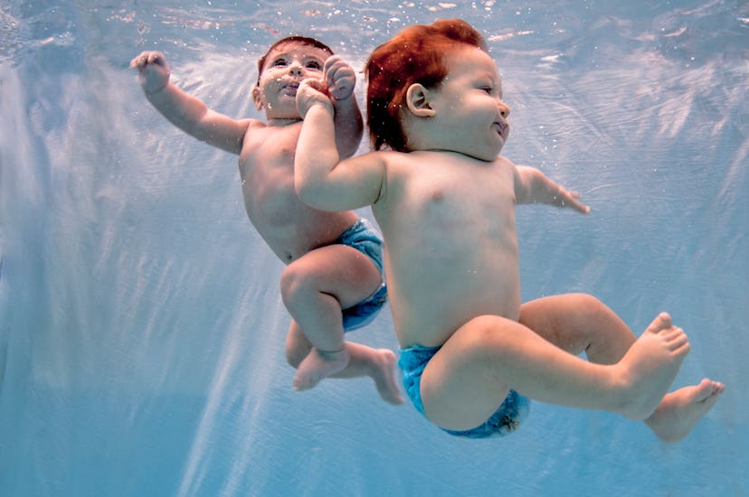 twin babies swim underwater holding hands