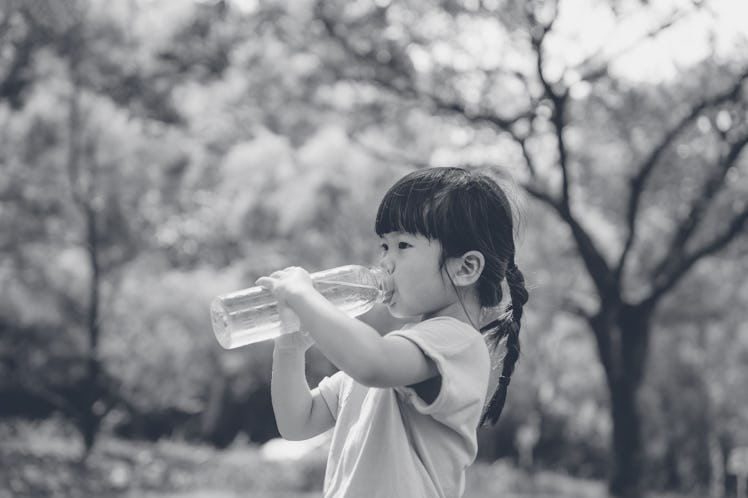 A little girl with pigtail braids drinks out of a huge clear plastic water bottle in the woods