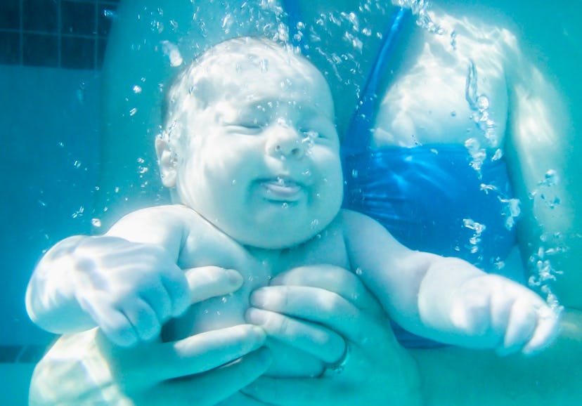 Mother dunking baby under the water during a swimming lesson at a swimming pool