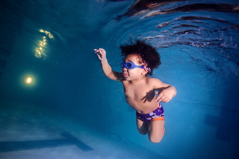 Underwater baby with curly Black hair in blue goggles and blue swim trunks