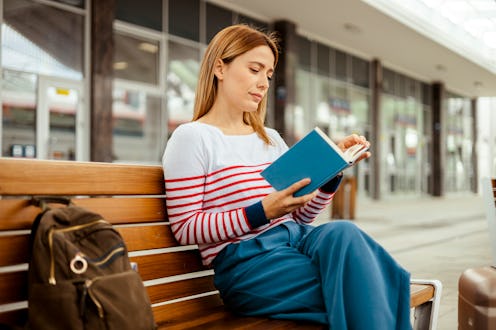 Young woman reading book, waiting at train station. Travel and active lifestyle concept.