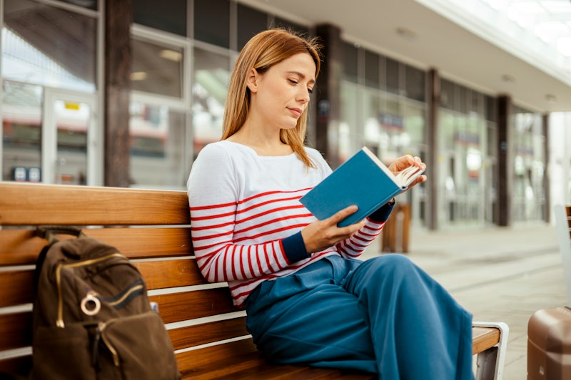 Young woman reading book, waiting at train station. Travel and active lifestyle concept.