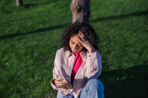 High angle view of curly teenage girl sitting in a park and scrolling her smartphone.